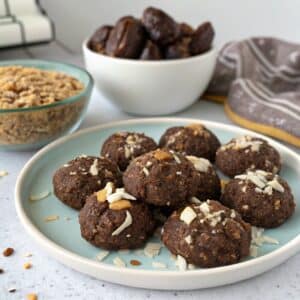A plate of healthy no-bake cookies with a natural, rustic look, next to a bowl of mashed banana and dates.